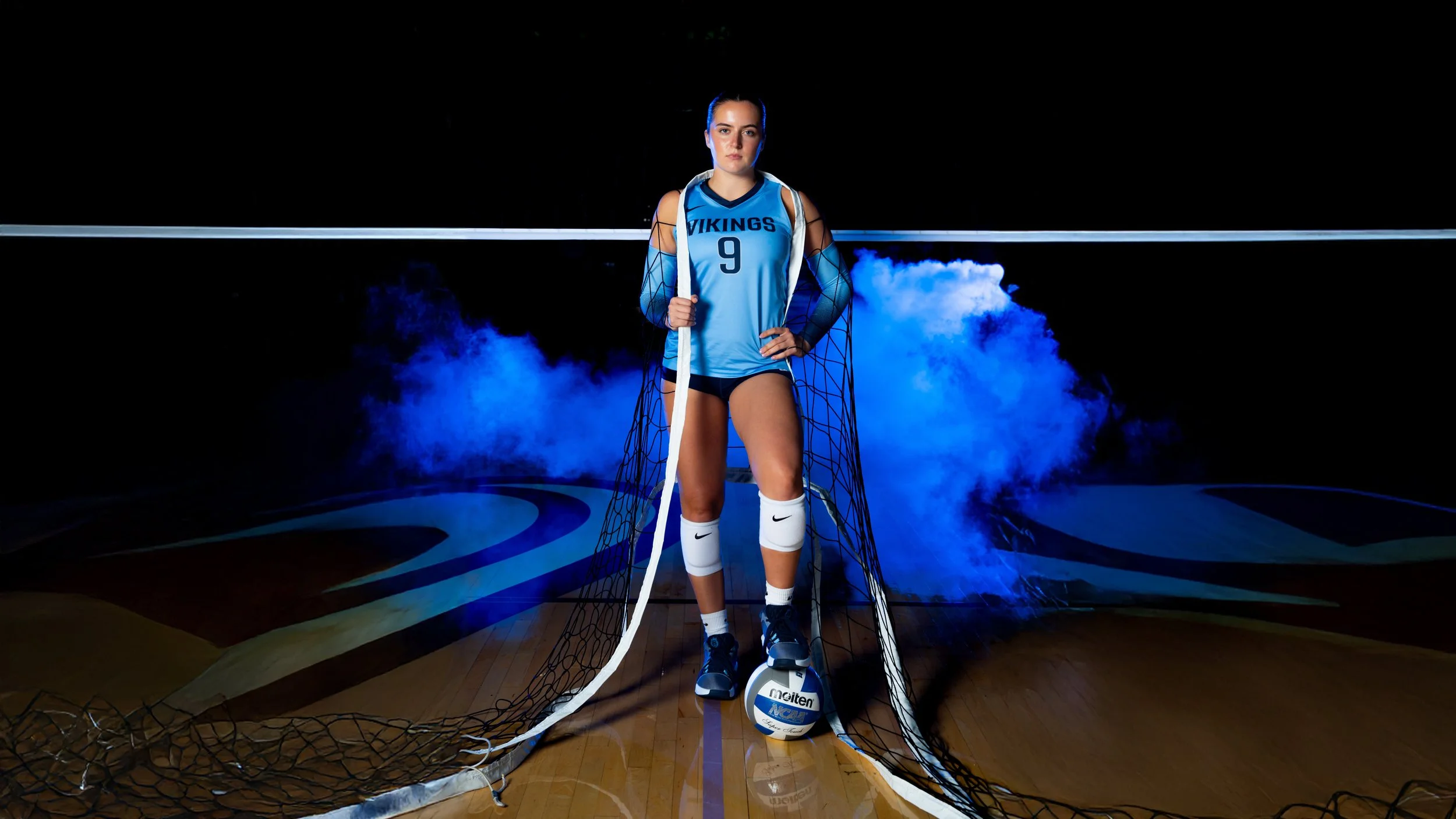 Vikings volleyball player posed on the court with blue stage smoke